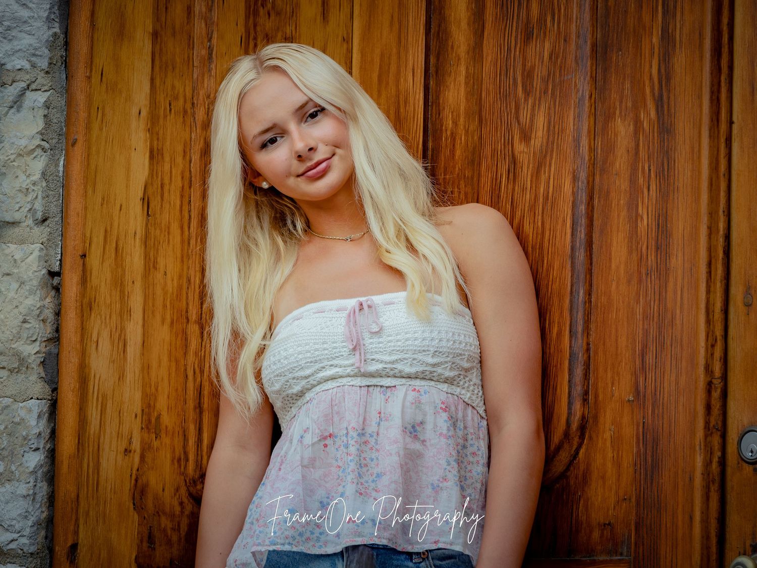 A person in a white strapless top poses against a rustic wooden door in an outdoor setting.