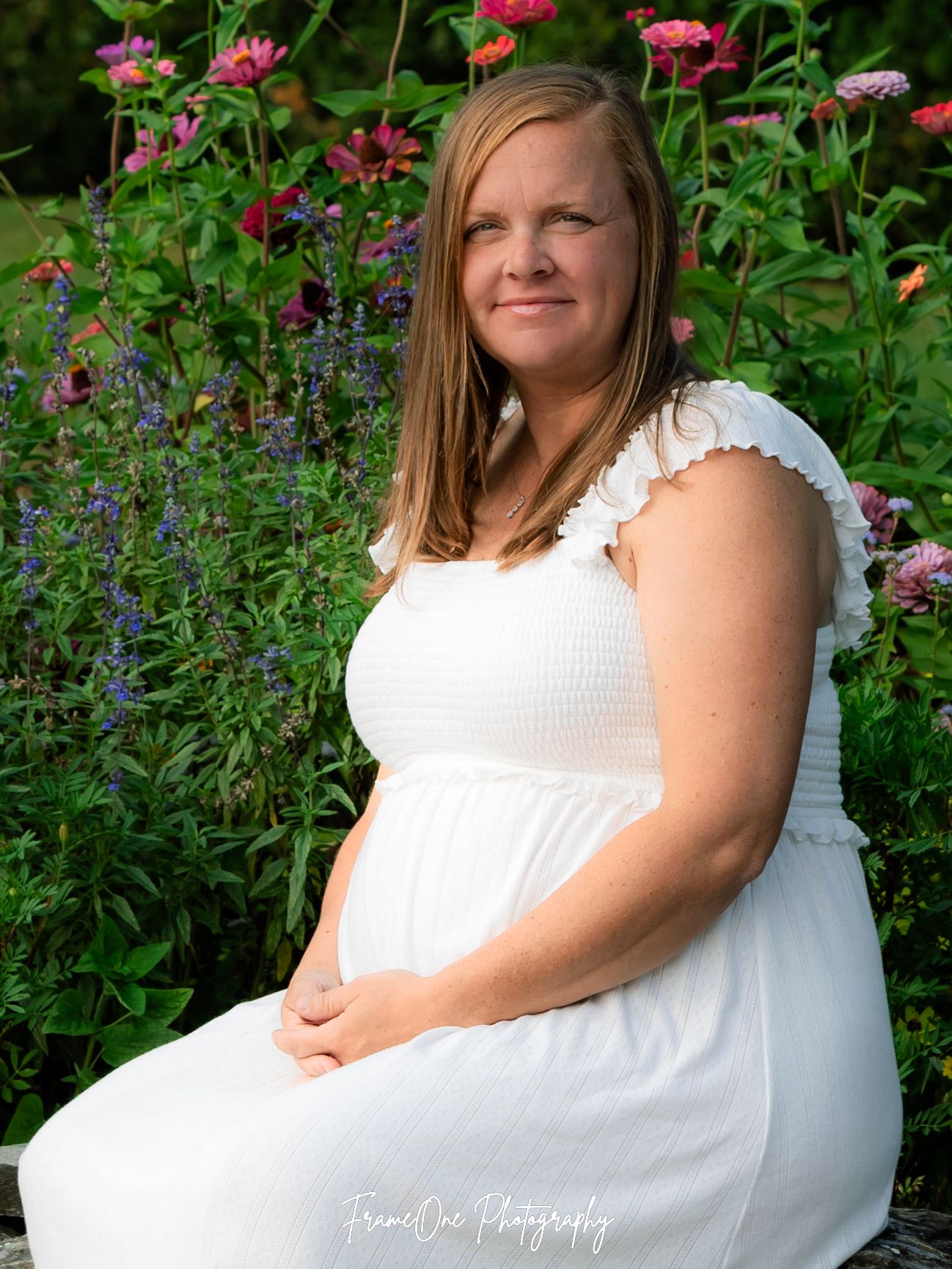 A figure in a white dress sits peacefully among vibrant pink and purple flowers in a lush garden setting.