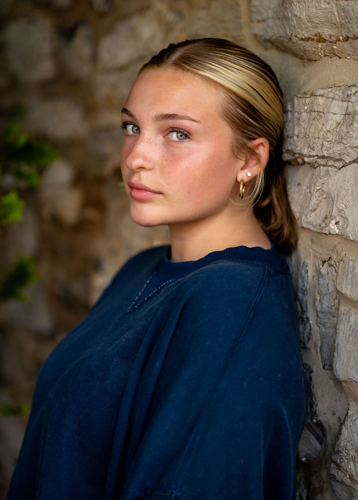 Close-up portrait of a person wearing a navy blue top against a stone wall.