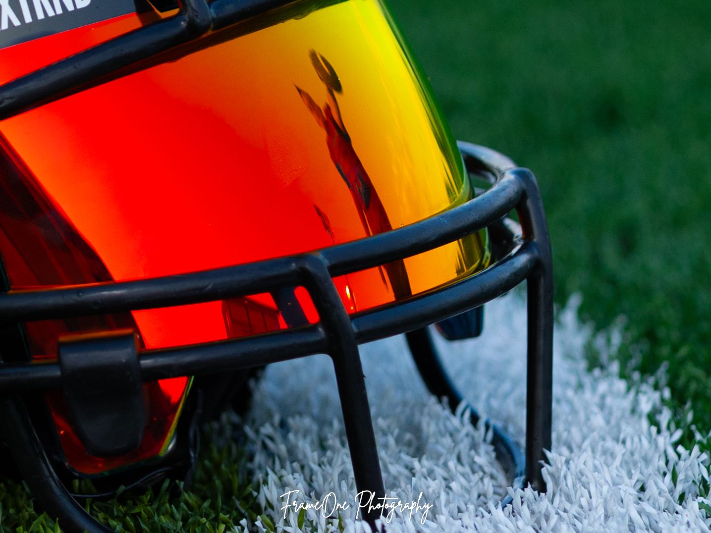 Close-up of football helmets with orange, black and green colors lined up on a grassy field.
