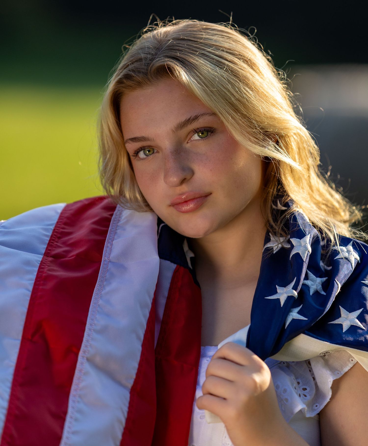 A person draped in an American flag stands in golden sunlight against a soft green background.