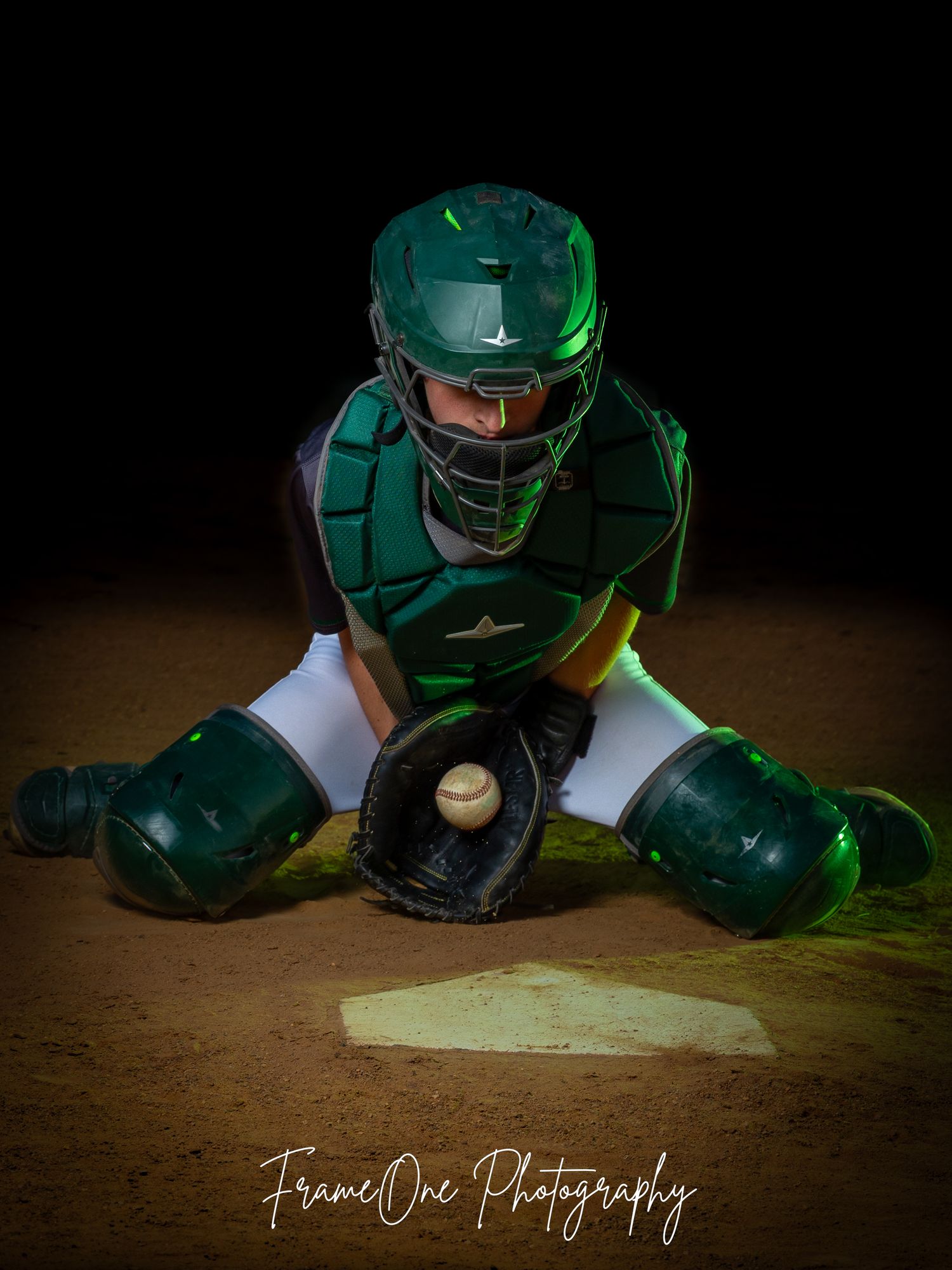 Baseball catcher's equipment laid out on dirt infield with dramatic green lighting and professional photography watermark.