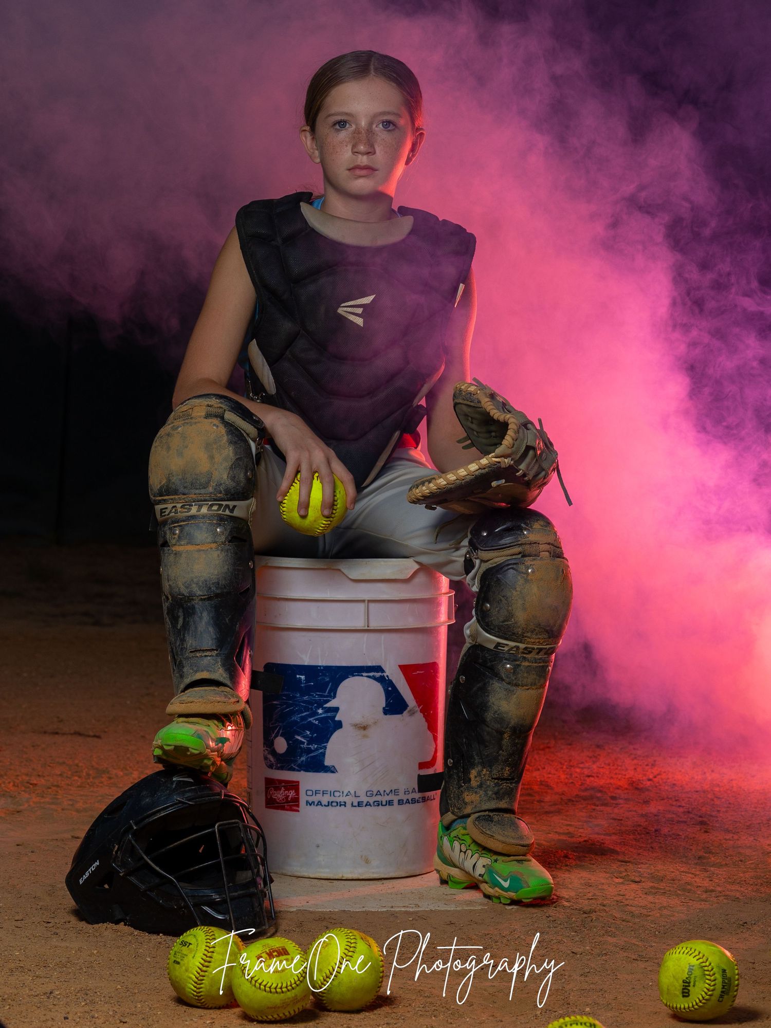 Dramatic softball player portrait with neon pink smoke and equipment against dark backdrop highlighting softballs and gear.