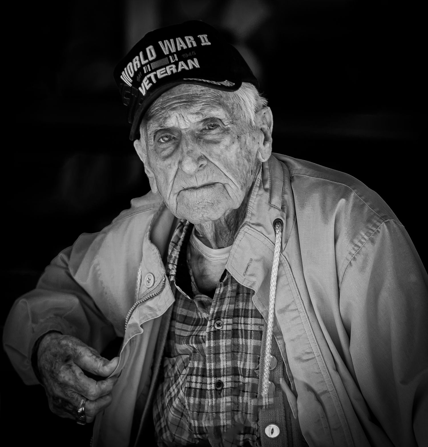 A black and white portrait shows a World War II veteran wearing a military cap and plaid shirt.