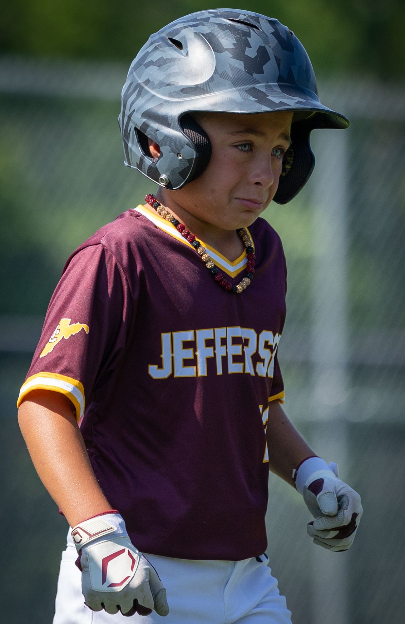 A youth baseball player in a maroon Jefferson jersey and gray batting helmet standing ready at the plate.
