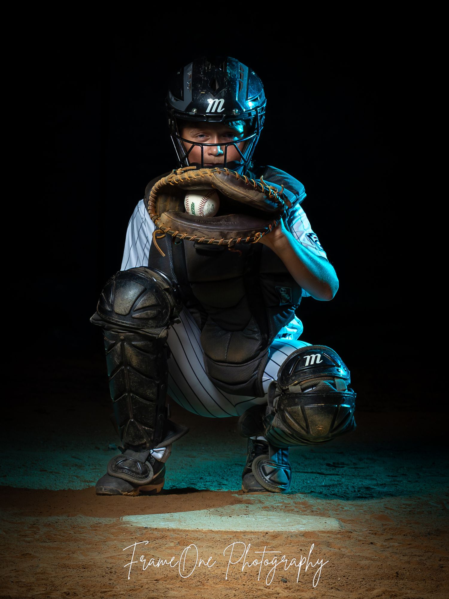 A baseball catcher in dark gear with blue lighting crouches in position against a dramatic black background.