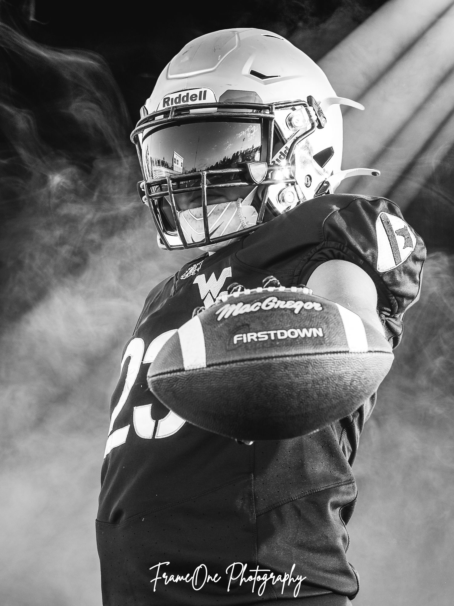 A football player in white and black gear holds the ball during practice in dramatic black and white lighting.
