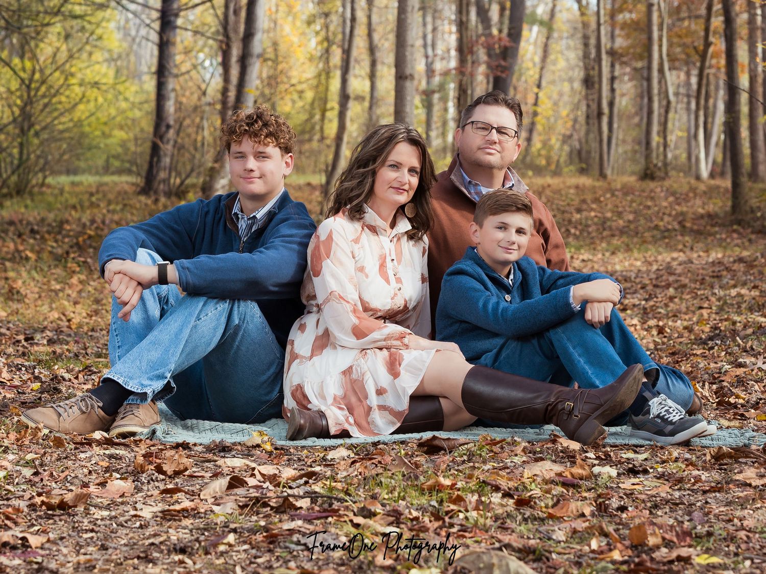 A group relaxes together on a blanket surrounded by fallen autumn leaves in a wooded setting.