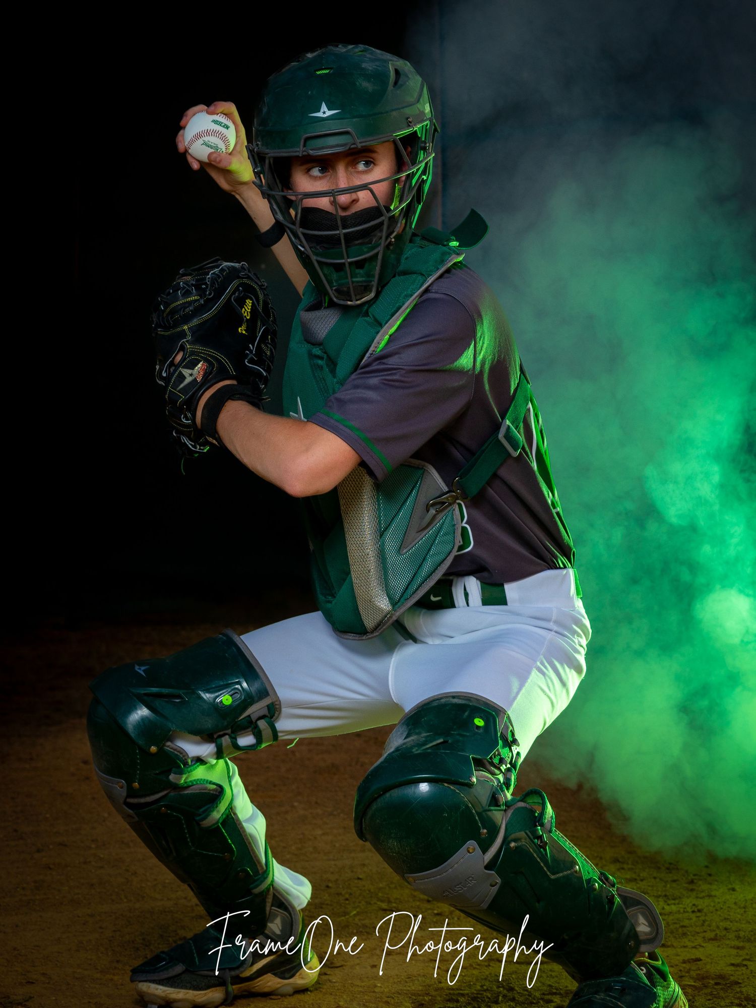 Baseball catcher in dark green gear poses dramatically with green smoke effects in professional sports photography.