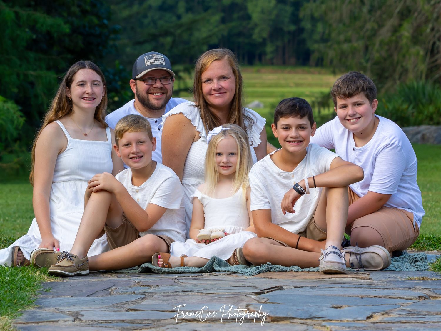 A happy family wearing coordinated white outfits poses casually on a wooden deck during an outdoor photo session.