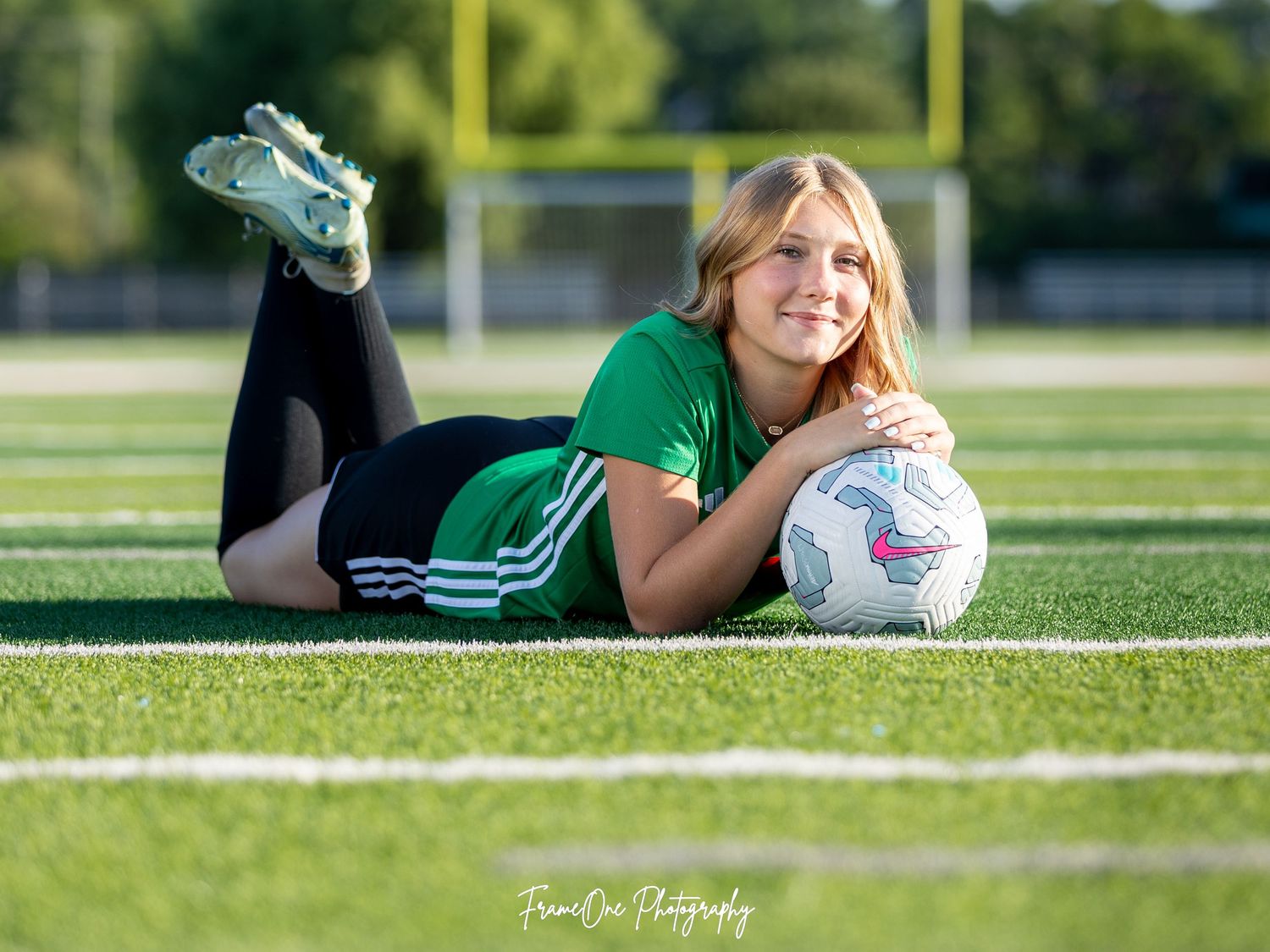 Soccer player lying on green grass field with ball during sunny day photoshoot.