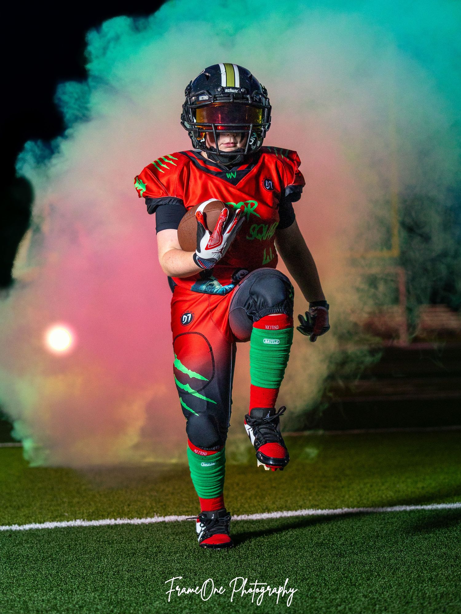 Football player in red uniform runs through dramatic colored smoke on field during dramatic sports photography shoot.