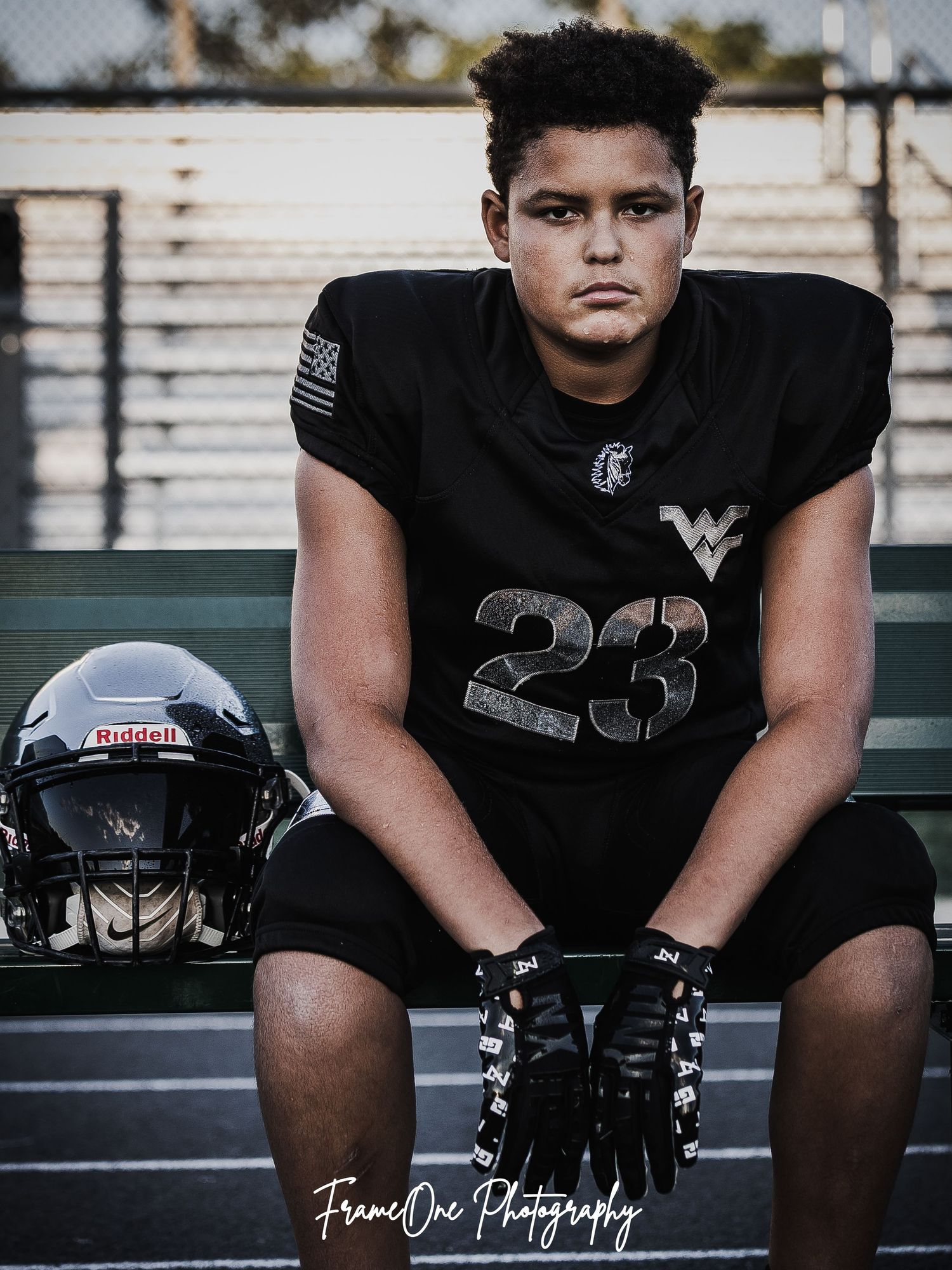 High school football player in black uniform seated on bench in dramatic sports photography series.