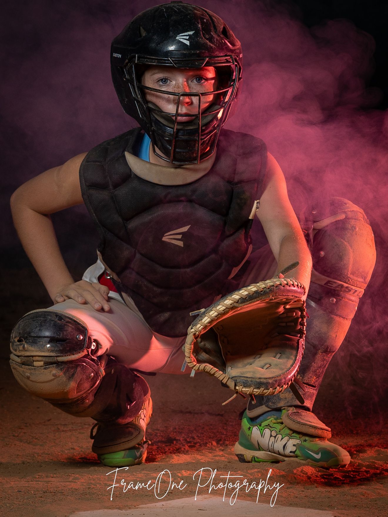 Baseball catcher in protective gear crouches in dramatic pose with red smoke effect and dramatic lighting.