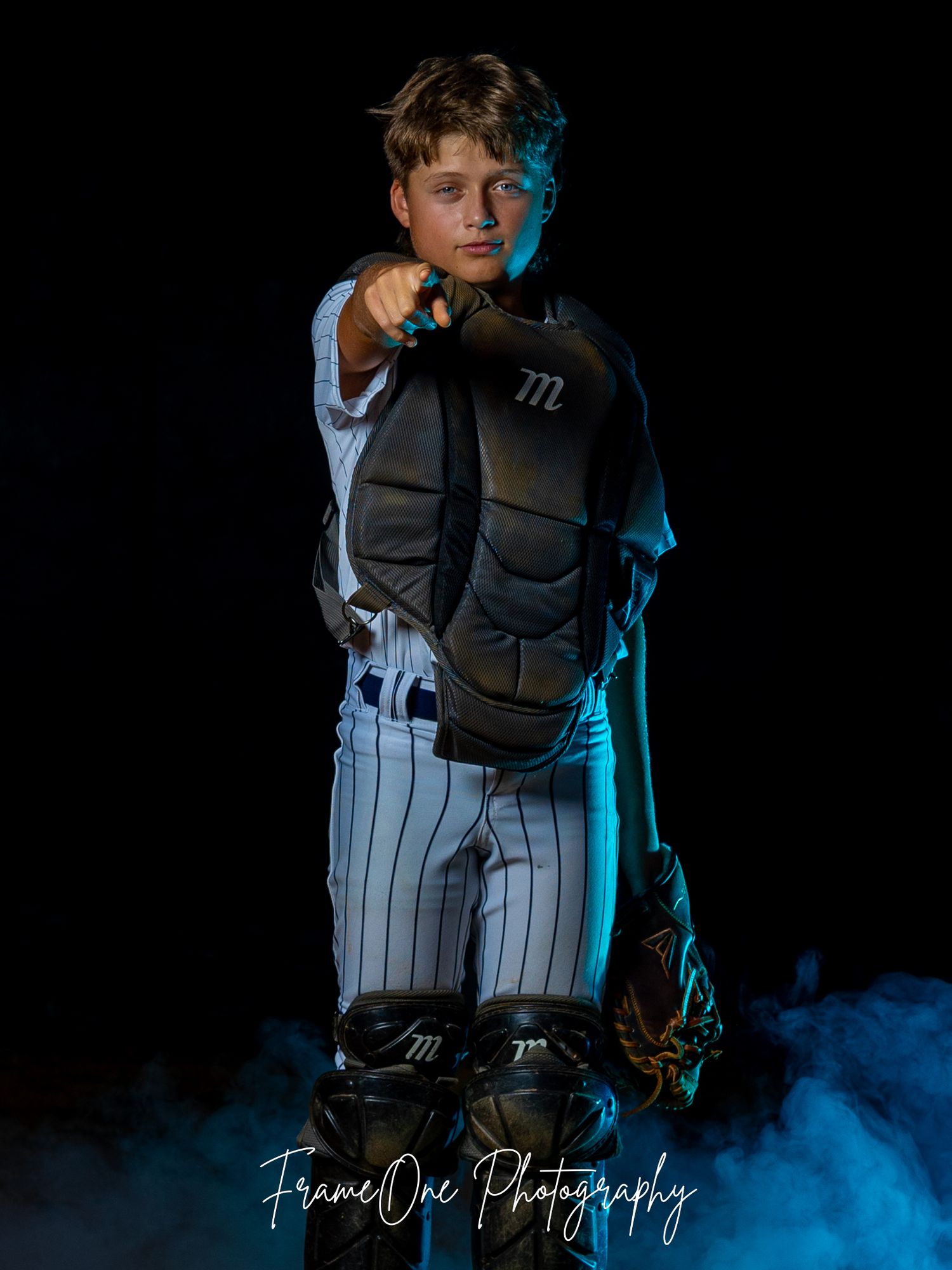 A baseball player poses in a pinstriped uniform and protective gear against a dark background with dramatic blue lighting.