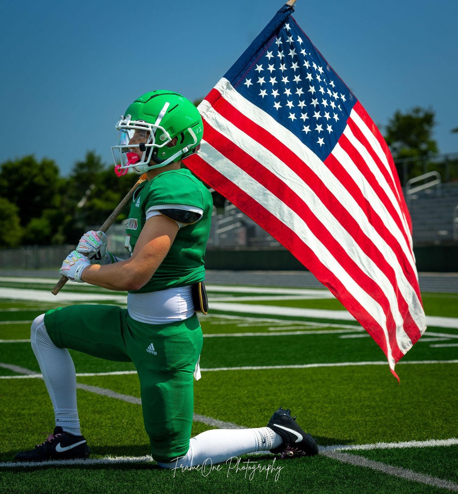 Football player runs with American flag on field during patriotic pre-game ceremony.