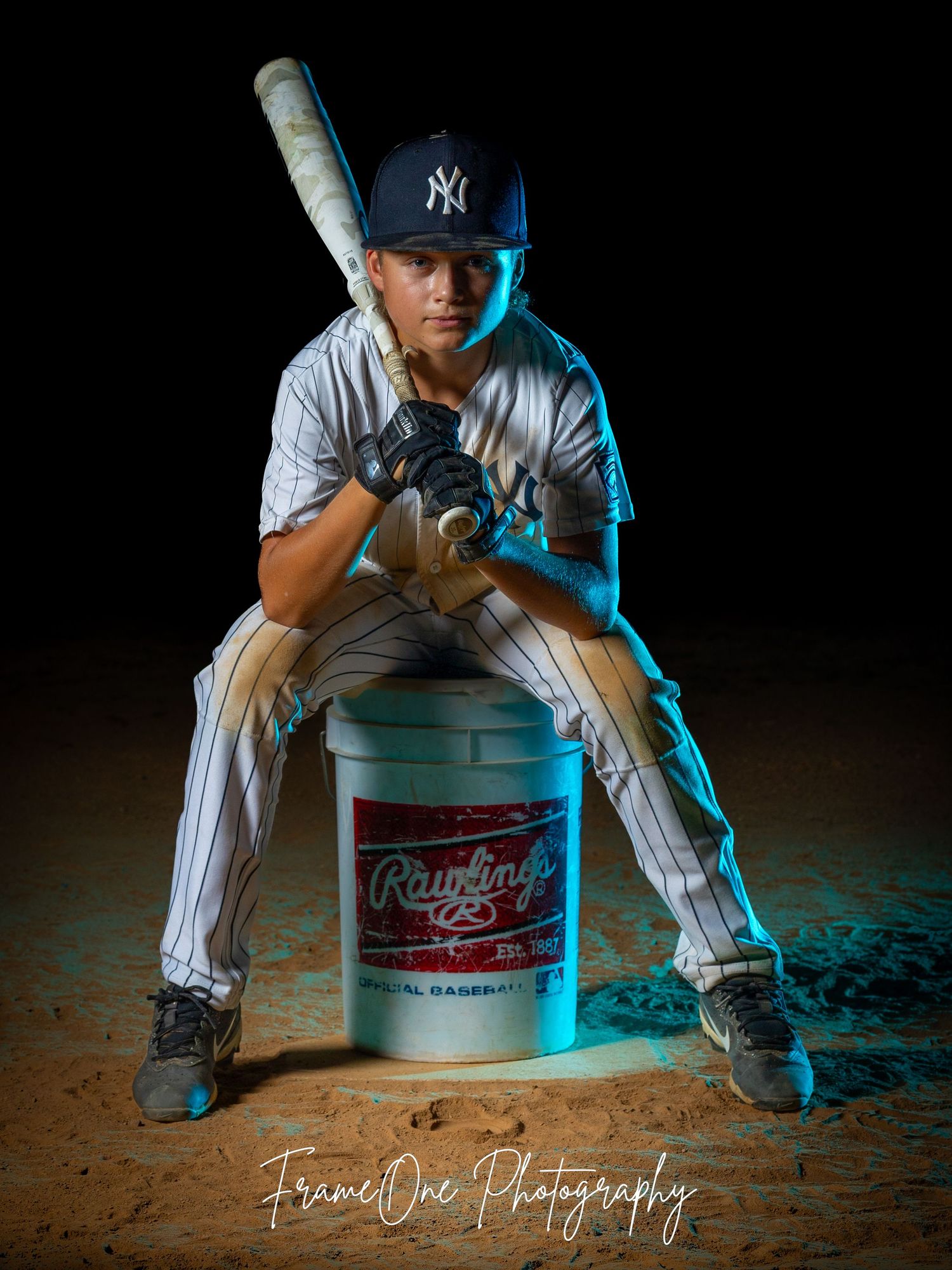 A baseball player in pinstripes sits on a Budweiser bucket against a dramatic black background with blue lighting.