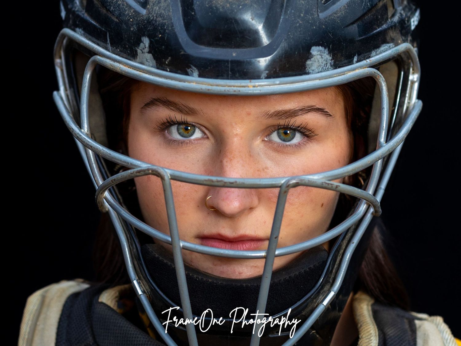 A close-up view of a person wearing protective athletic gear including a helmet with a face mask against a dark background.