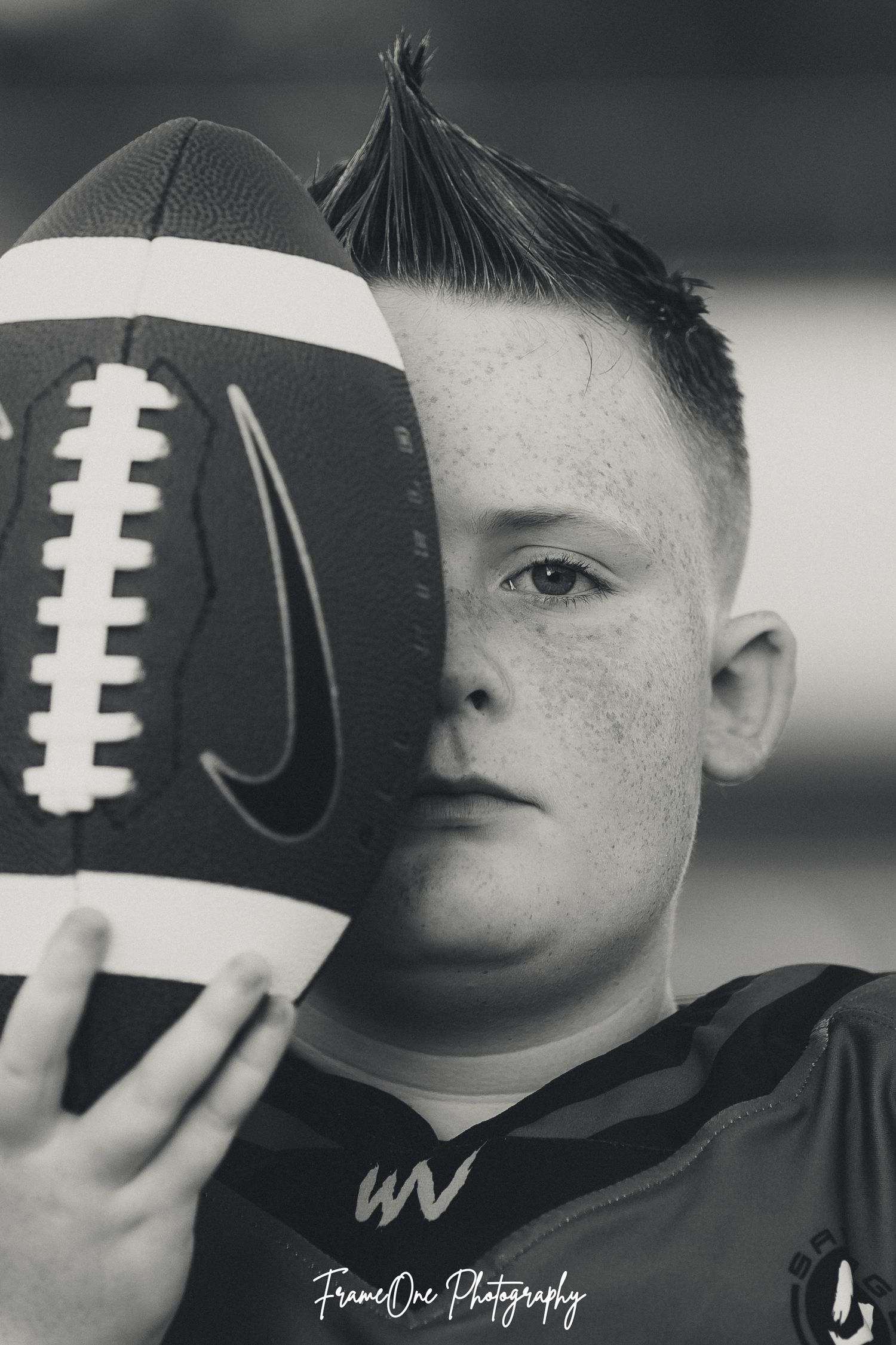 Black and white sports portrait with football showing partial view through dramatic lighting.