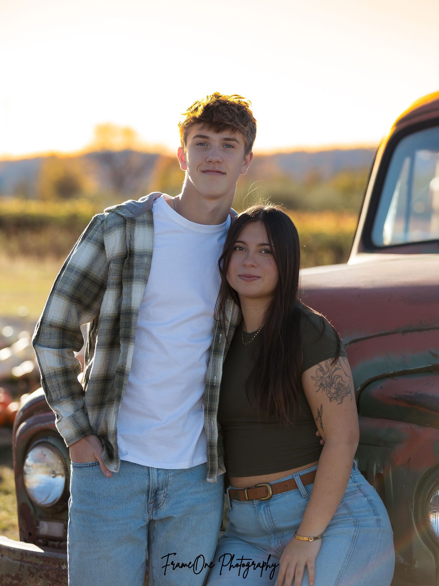 A couple poses together in front of a vintage truck during golden hour in a rustic outdoor setting.