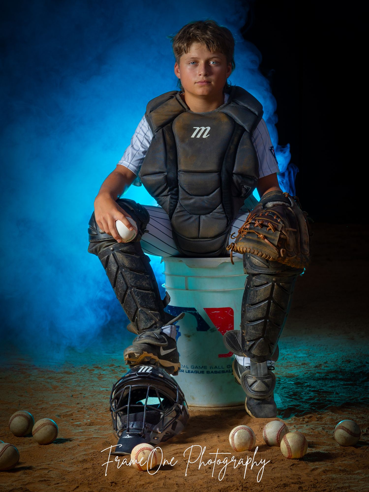 Baseball player in protective catcher's gear crouches with equipment against dramatic blue backdrop.