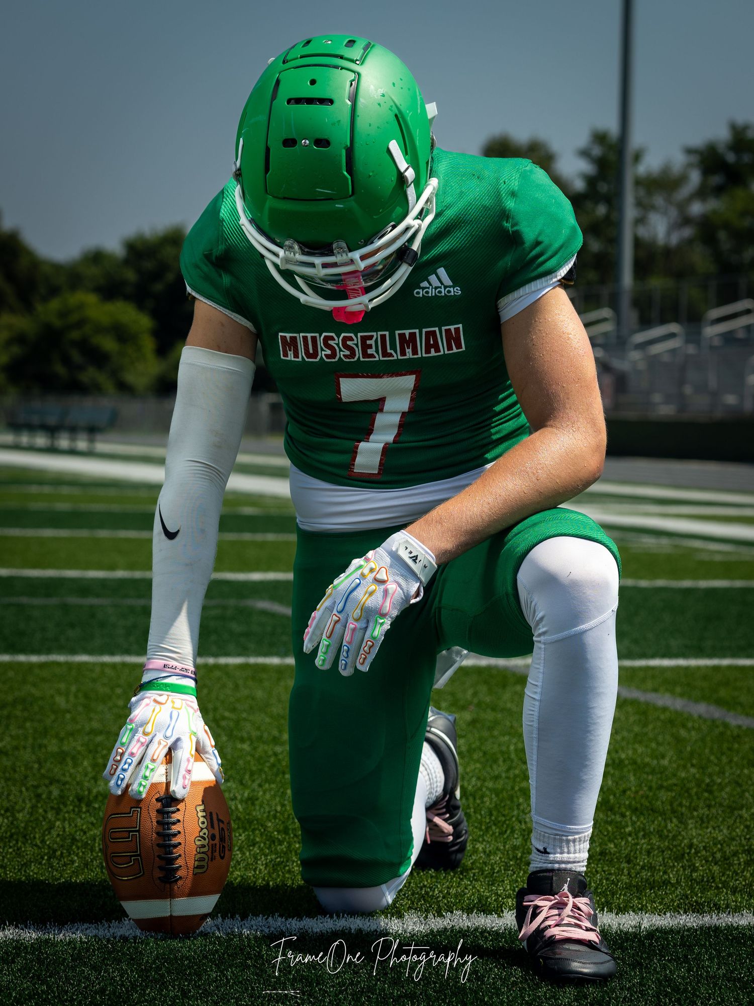 Football player in a green Missouri Western uniform kneels on field with football during game day photo shoot.