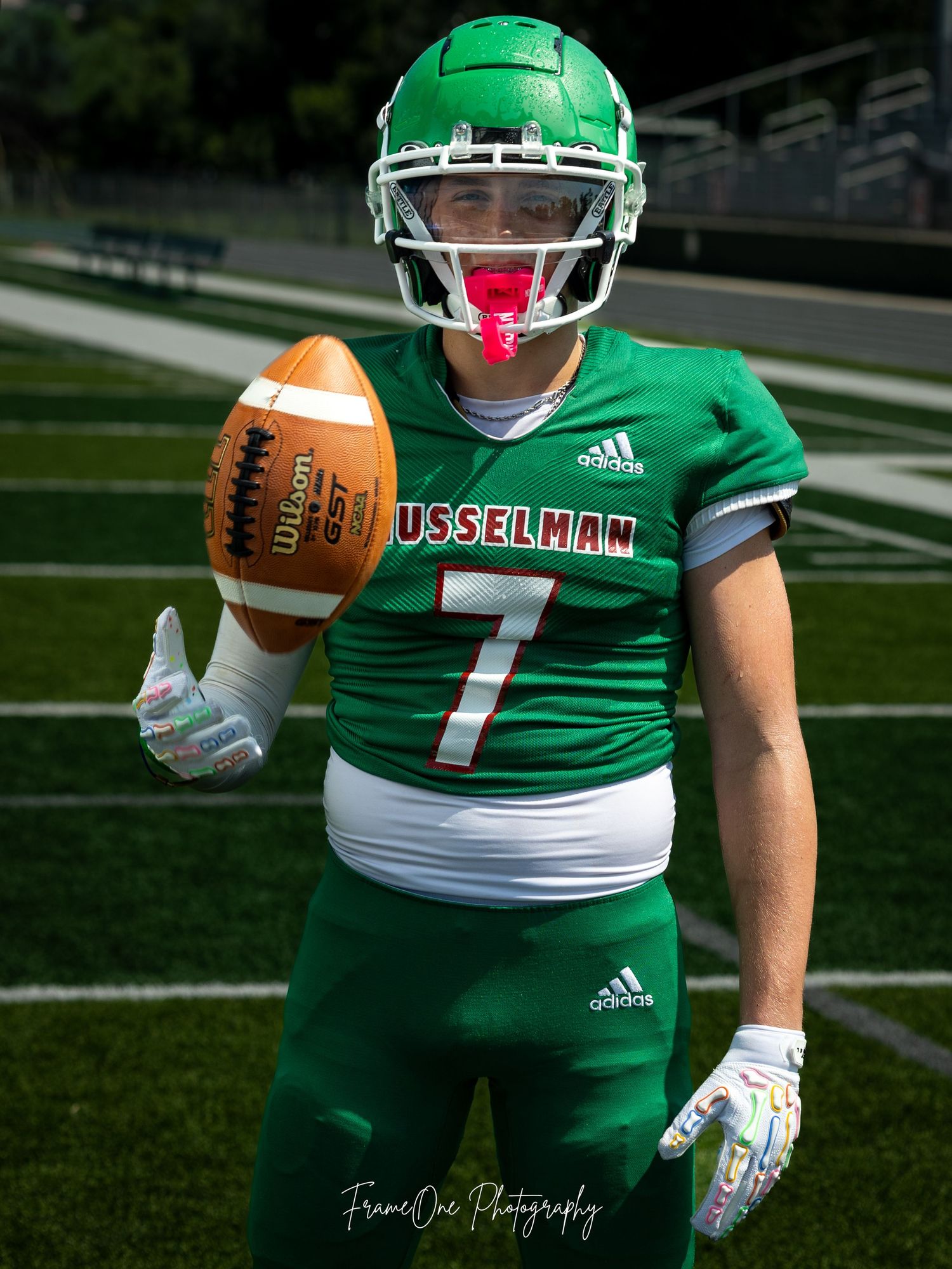 Football player in green Musselman uniform number 7 poses on field holding football with Adidas gear.
