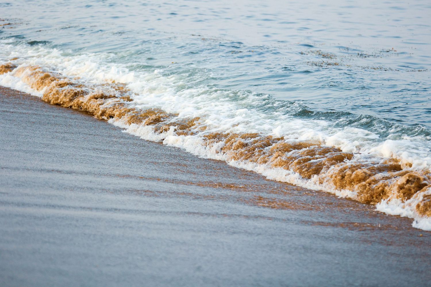 Waves gently rolling onto a sandy beach during a peaceful day at sea.