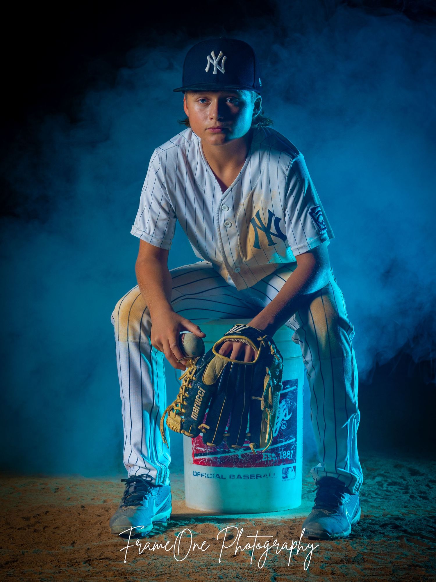 Baseball player in Yankees uniform poses with glove against moody blue background lighting.