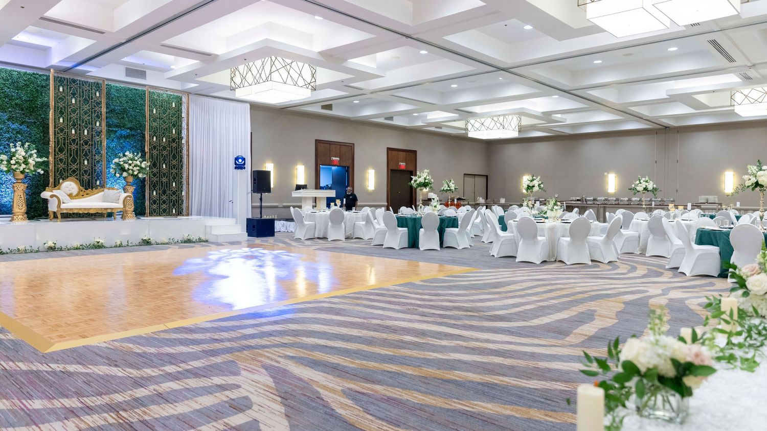 A panoramic view of an elegant banquet hall with crystal chandeliers and white table settings arranged for a formal event.