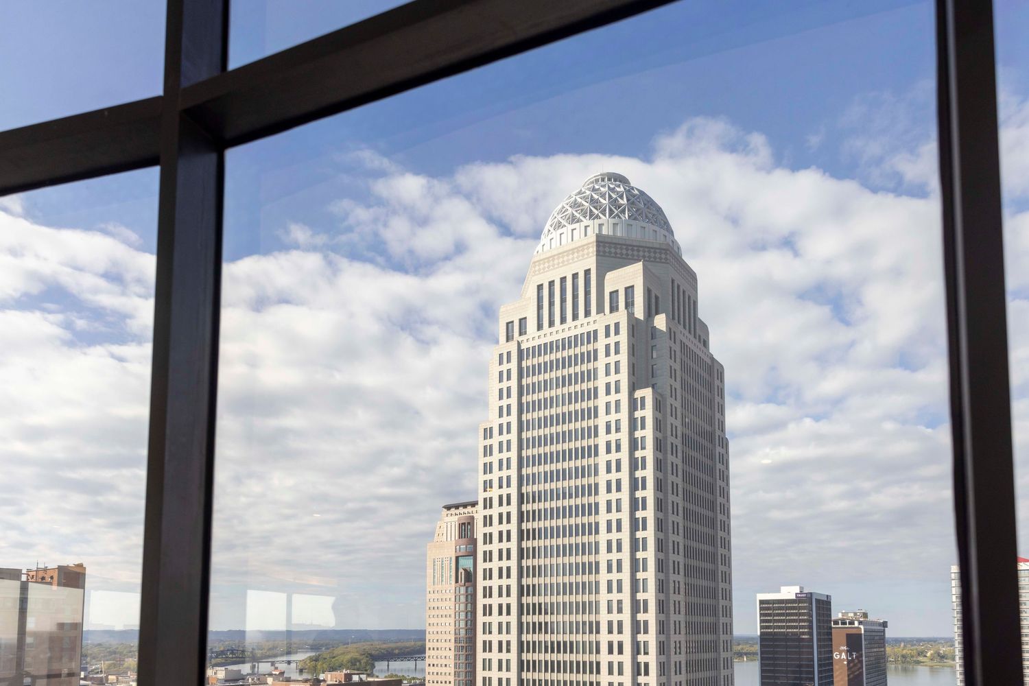 Art deco skyscraper with white limestone facade rises against blue cloudy sky, viewed through window frame.
