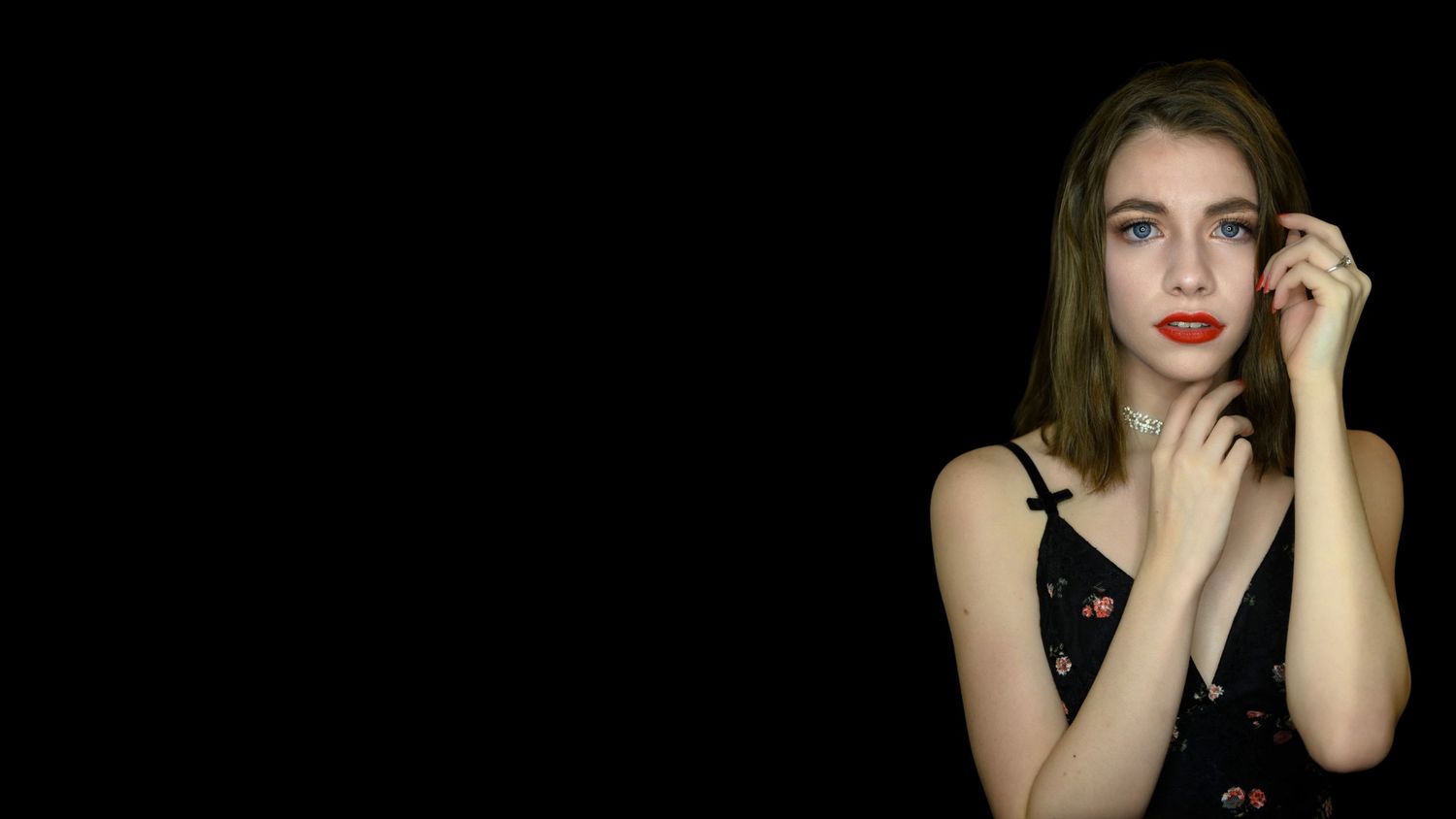 Dramatic portrait of a woman in black dress against dark background with red lipstick and long brown hair.