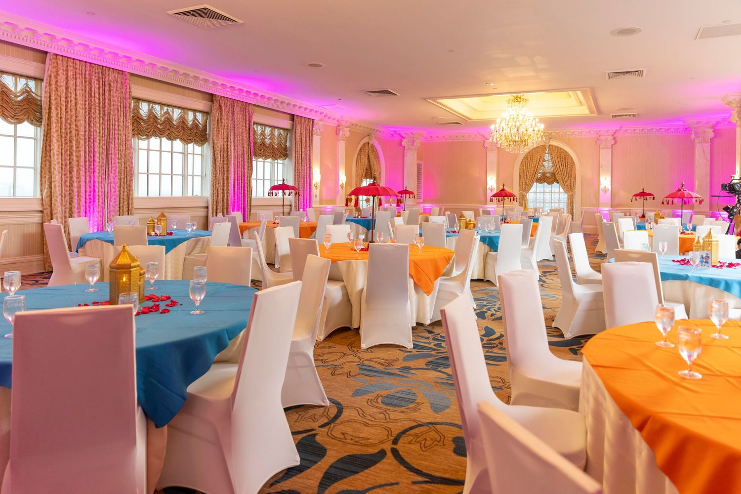 Elegant banquet hall decorated in pink uplighting with white chairs and orange table linens for a formal event.