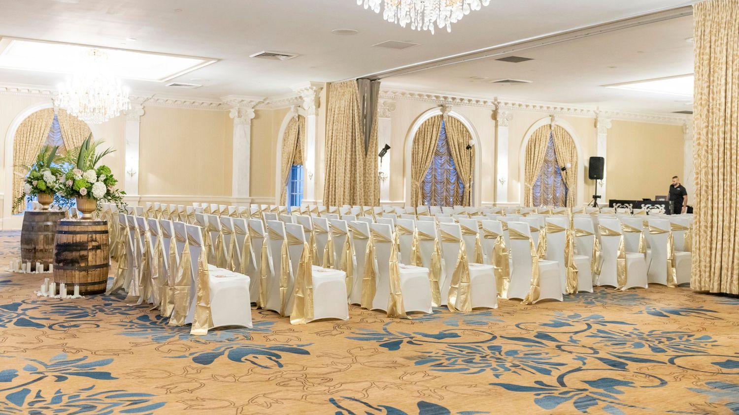 A panoramic view of an elegant wedding reception hall with crystal chandeliers and white-draped chairs.