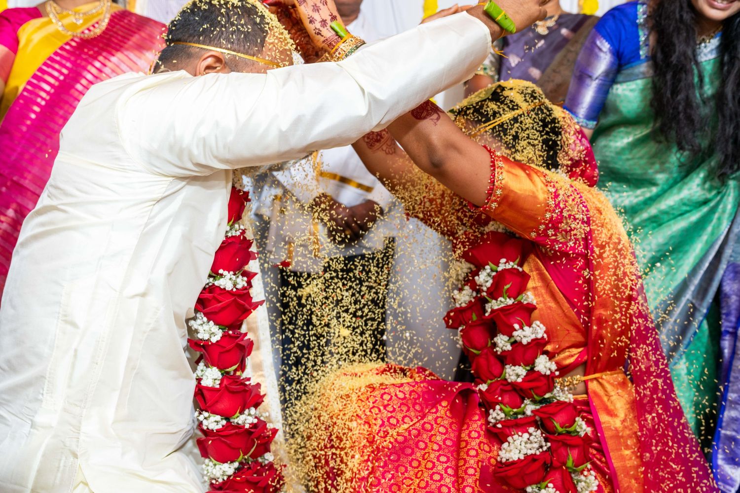 Colorful traditional Indian wedding ceremony with bride in red saree and groom in white exchanging garlands.