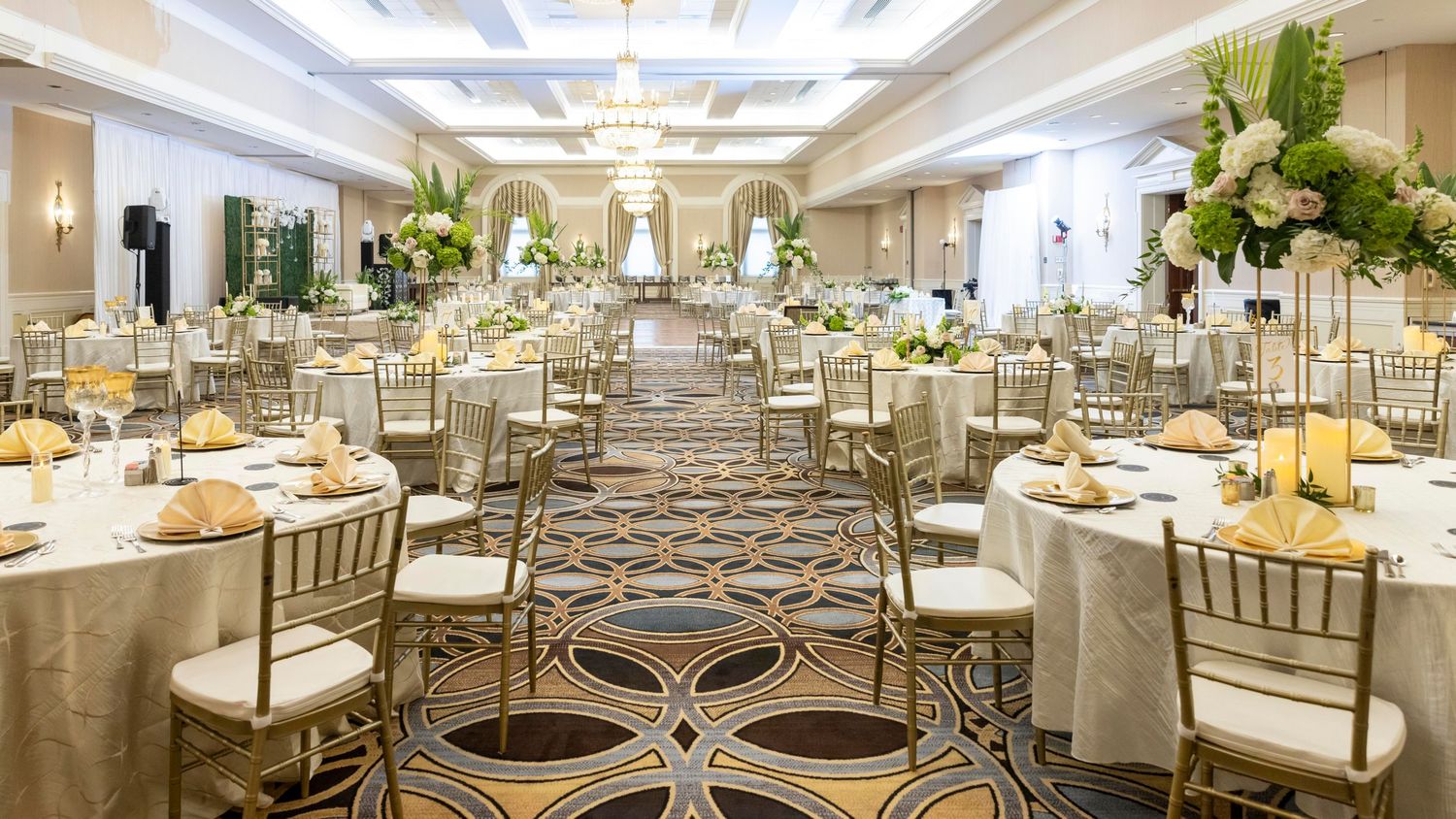 Elegant panoramic view of a luxurious wedding reception ballroom with crystal chandeliers and gold-accented table settings.