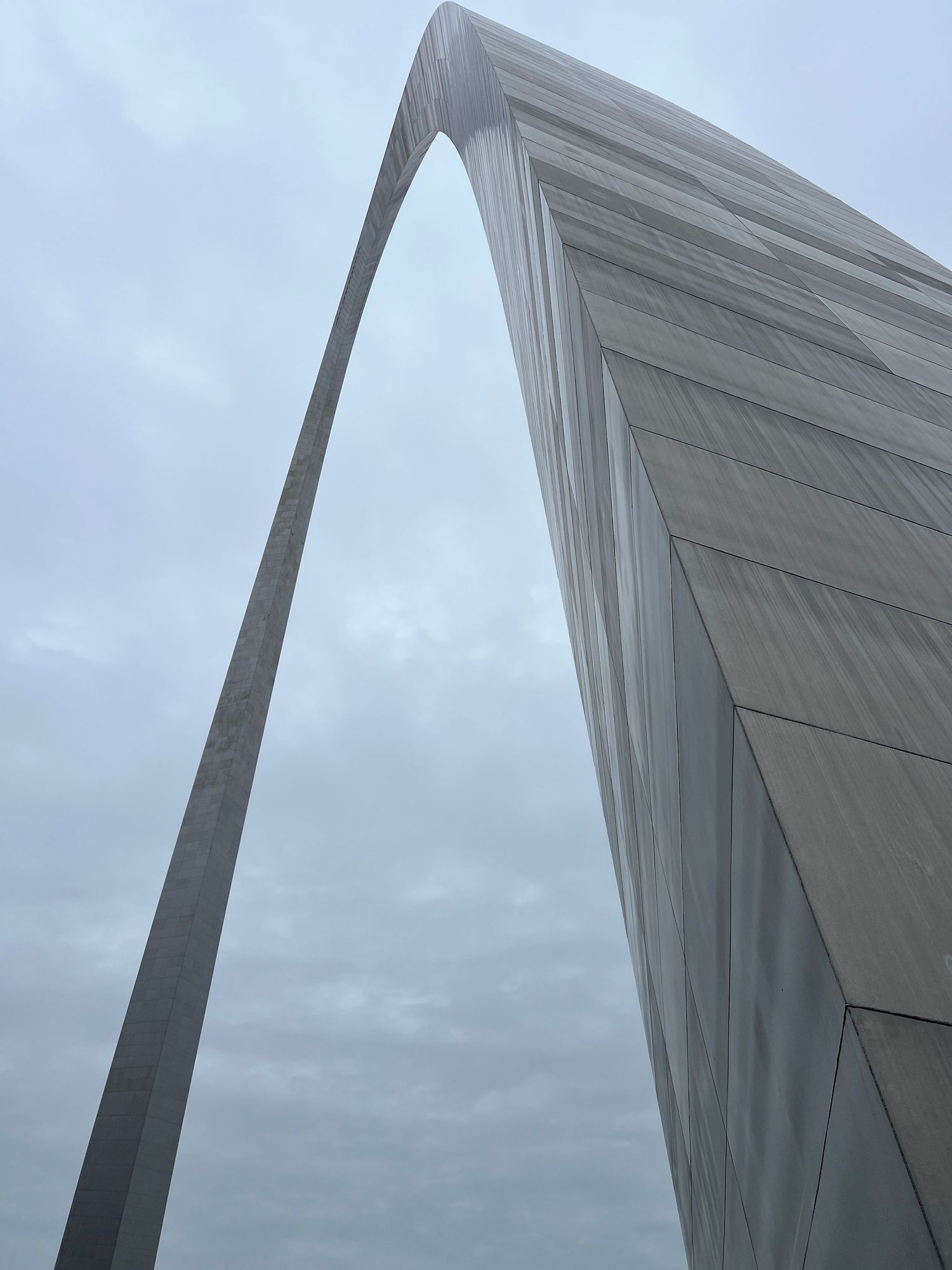 Dramatic upward view of the St. Louis Gateway Arch against an overcast sky.