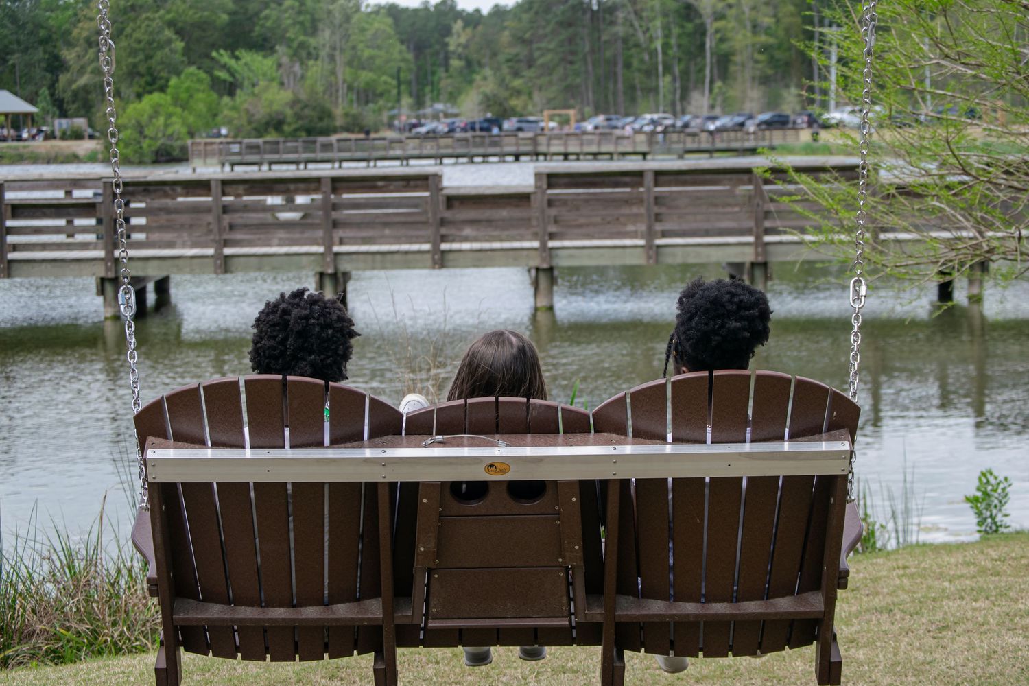 A photo of three girls sitting on a bench in front of a lake