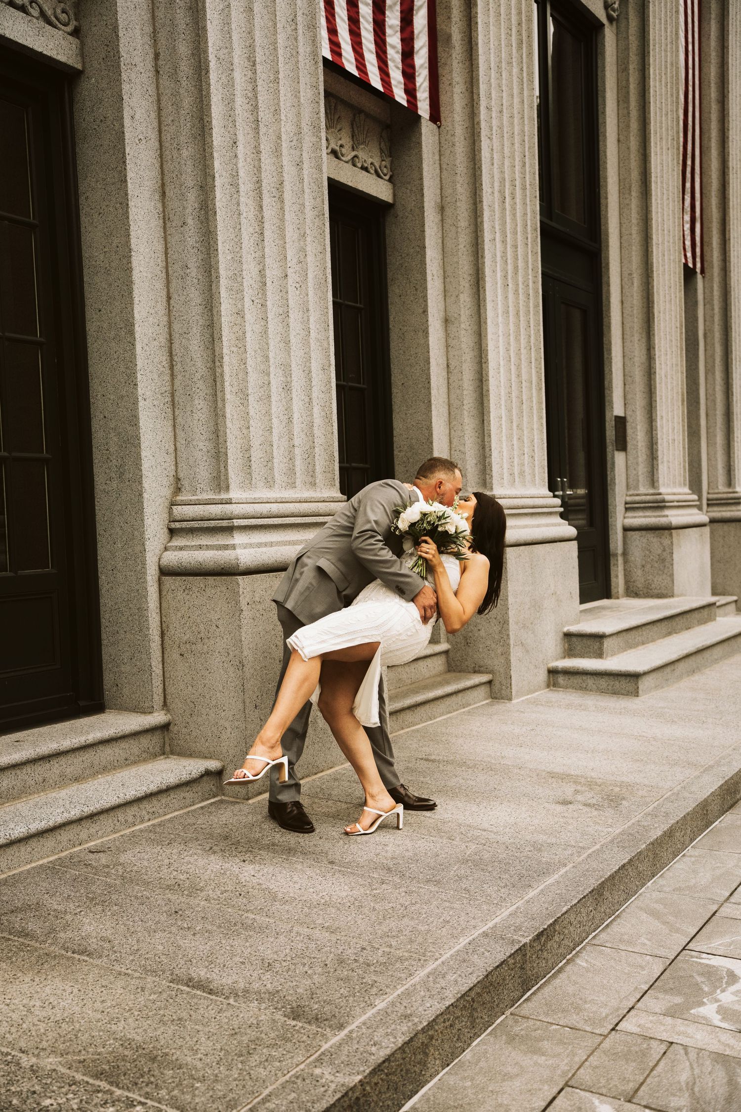 A classic romantic moment captured on steps of historic building with American flag in vintage sepia tones.