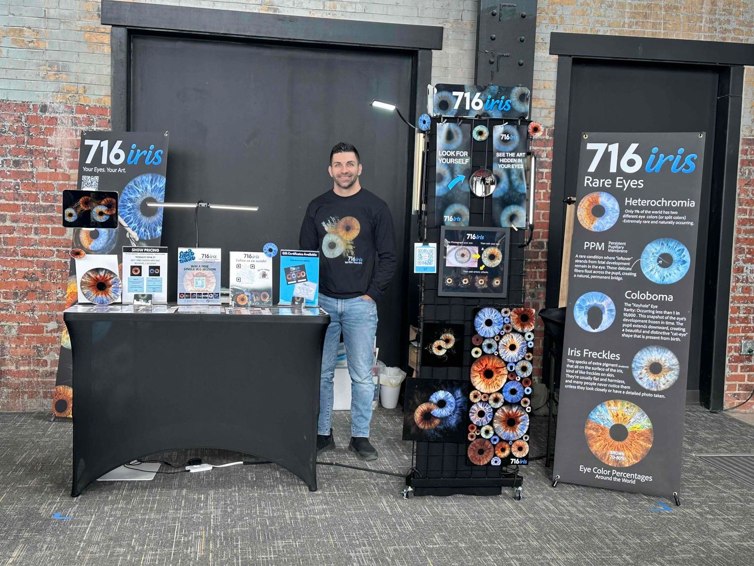 Man standing at a 716 Iris Rare Eyes informational booth displaying colorful eye condition diagrams and educational materials.