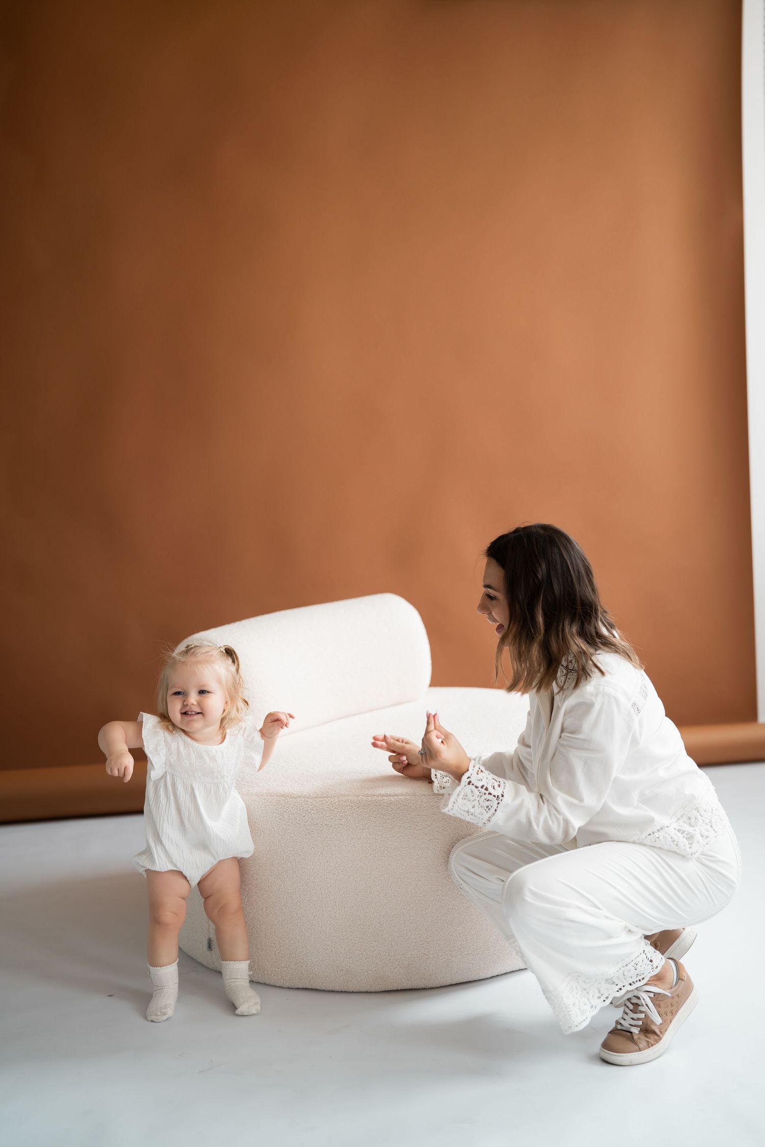 Mutter begleitet ihr Kleinkind bei den ersten Schritten im warmen Studio bei einem natürlichen Baby Fotoshooting in Berlin