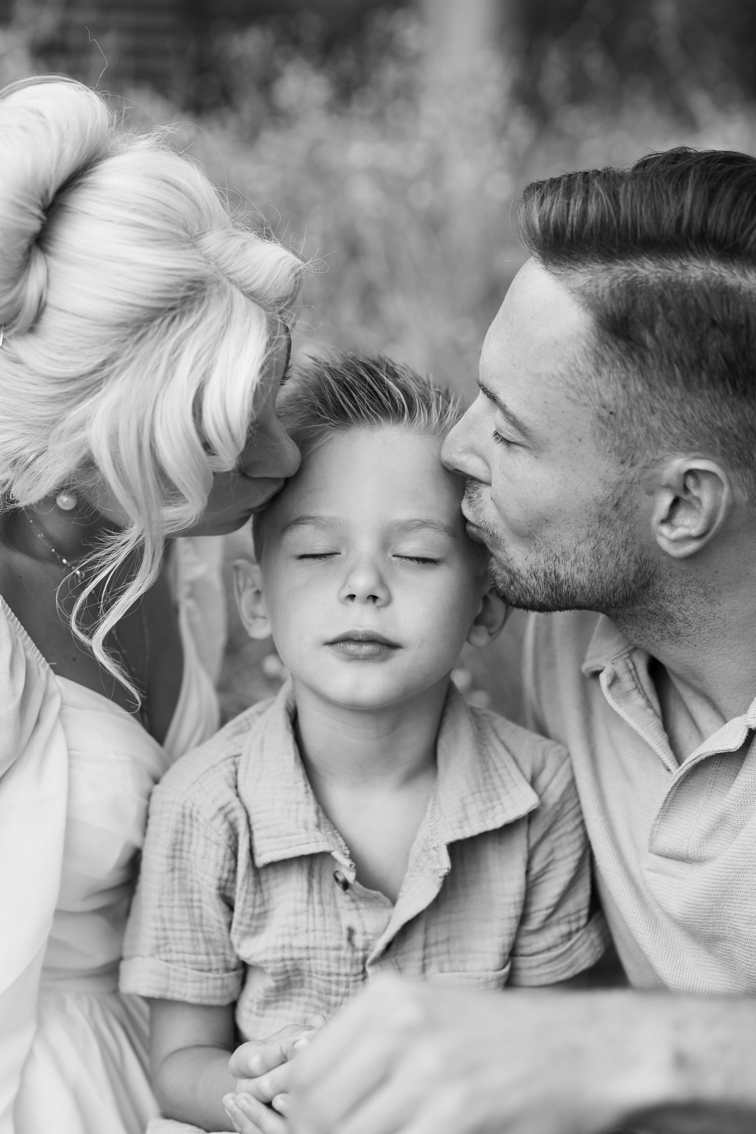Eltern mit dem Kind im Park – Eltern küssen ihr Kind zärtlich bei einem emotionalen Familien Fotoshooting in Schwarz Weiß im