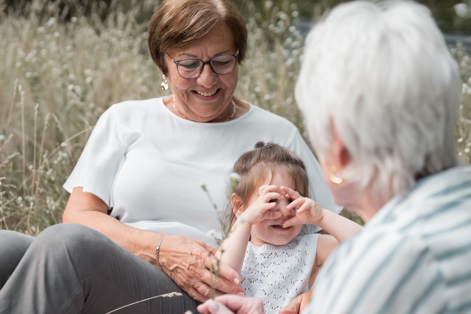 Großmutter mit Enkelkind im Sommer im hohen Gras bei einem natürlichen Familien Fotoshooting in warmer Atmosphäre