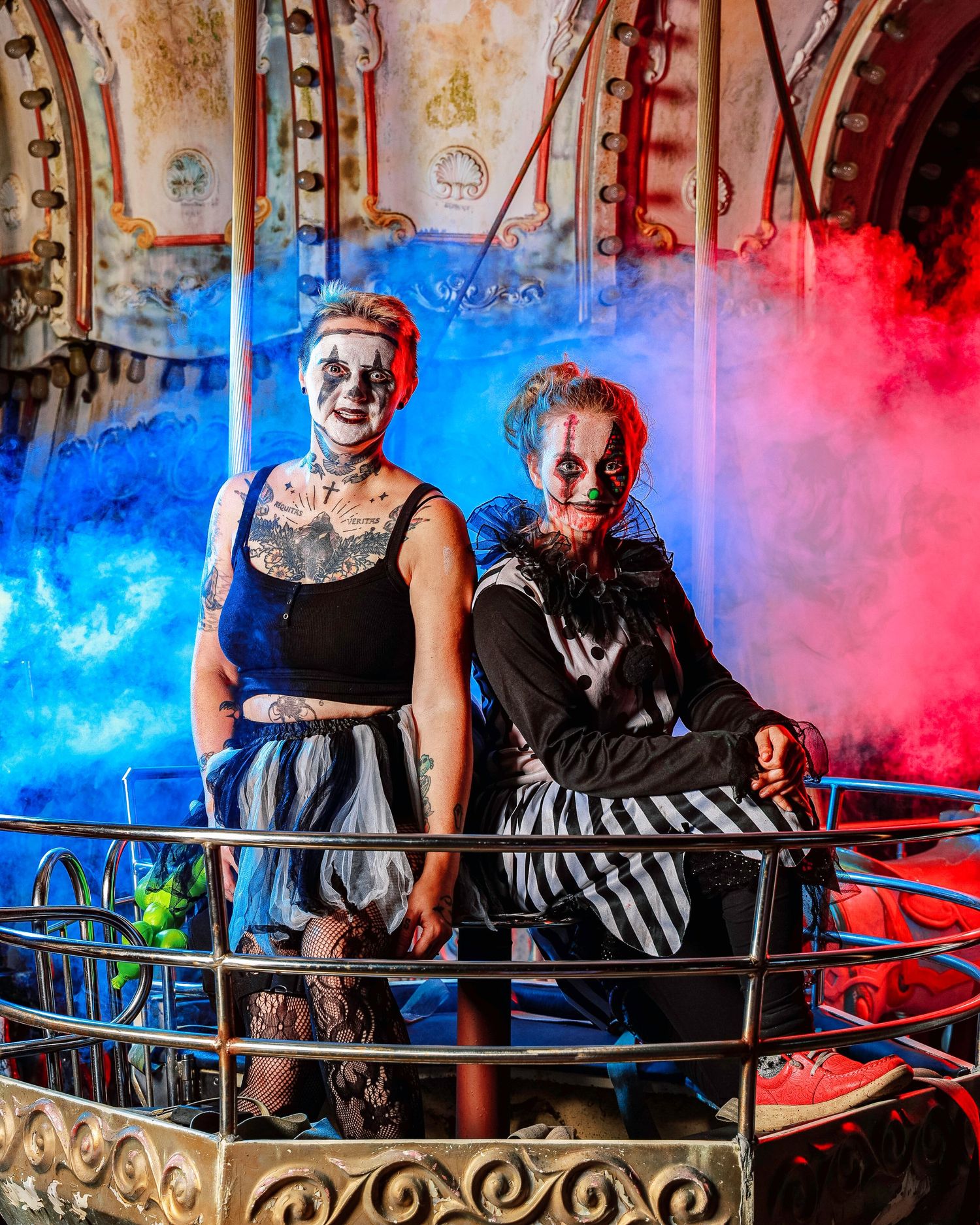 Two people pose together on an ornate balcony with dramatic red and blue lighting effects in the background.