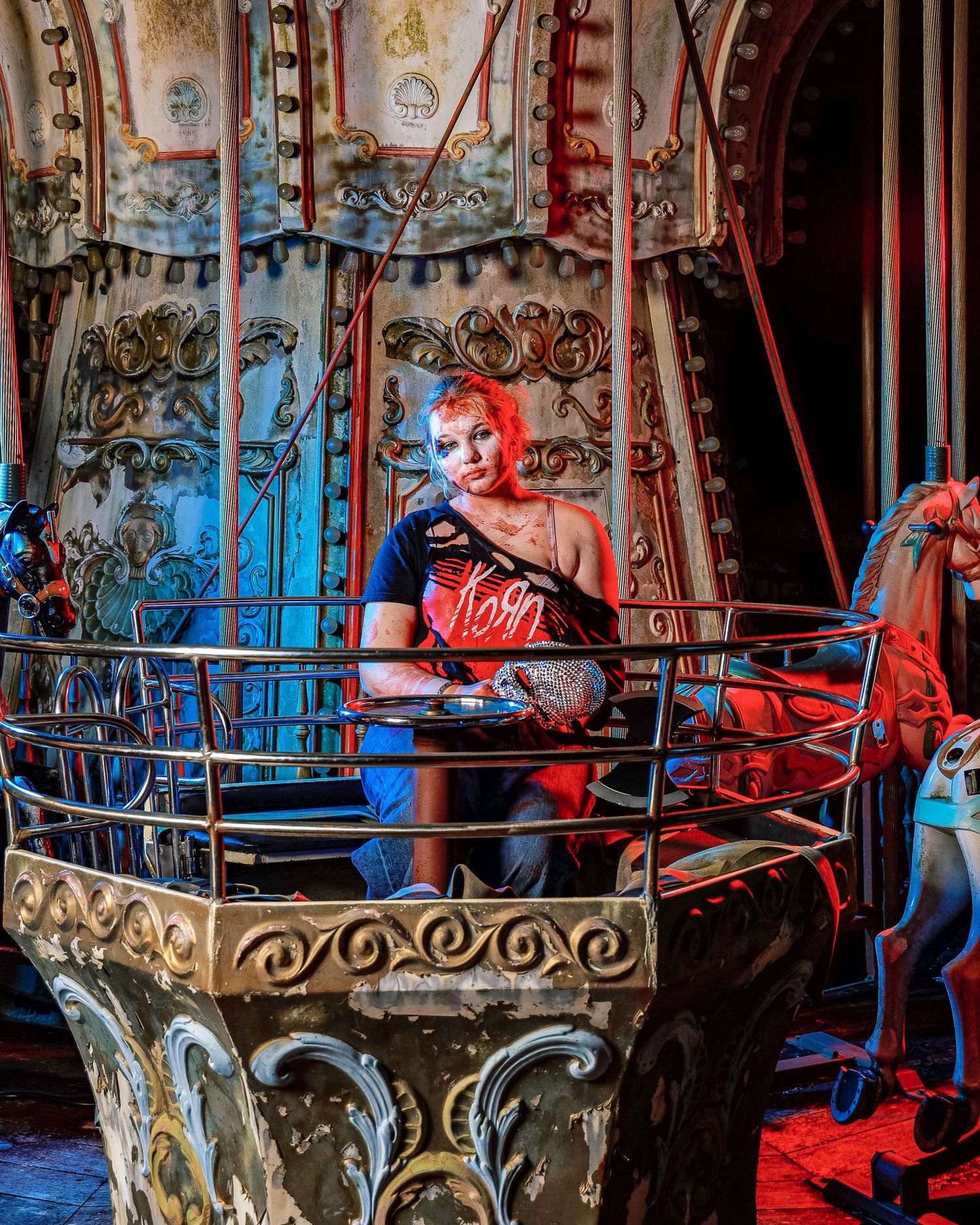 Abandoned carousel with ornate metalwork glows in dramatic red and blue lighting creating an eerie atmosphere.