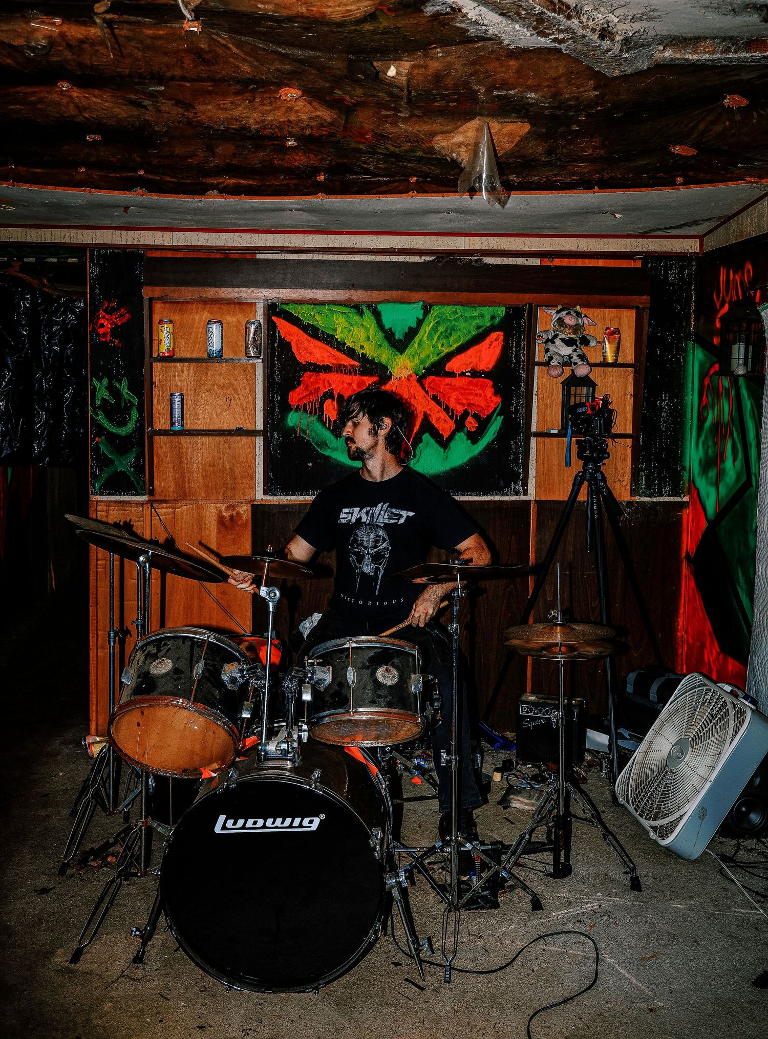 A sequence of dark concert venue photos showing a drum kit setup with dramatic red and green lighting on wooden walls.