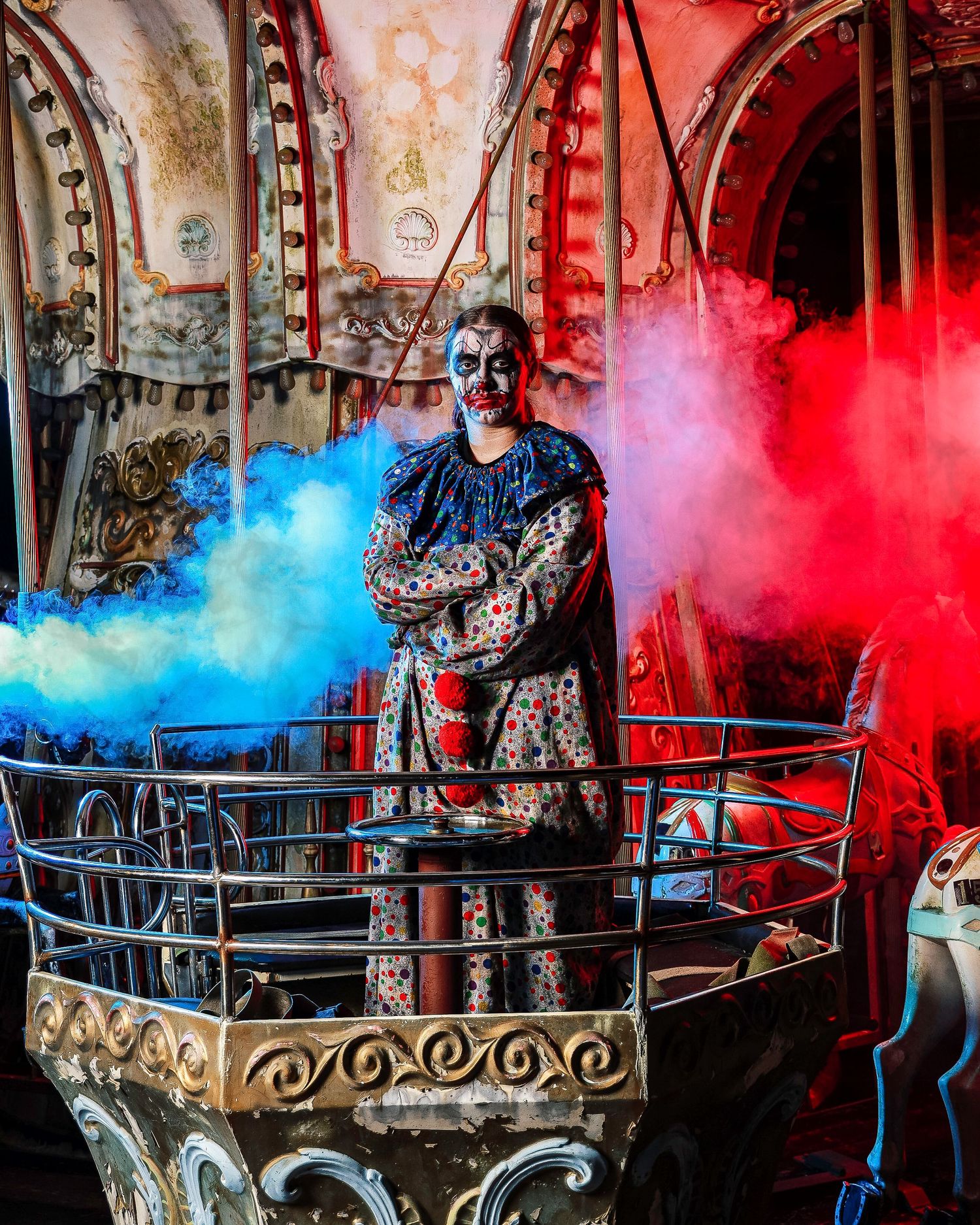 A person in gothic attire poses dramatically with colored smoke effects in a vintage industrial setting.