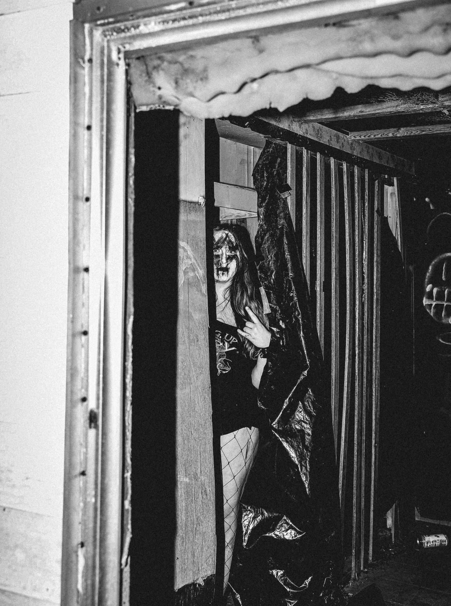 A black and white photo showing a dark corridor with vertical bars and hanging coats creating an eerie atmosphere.