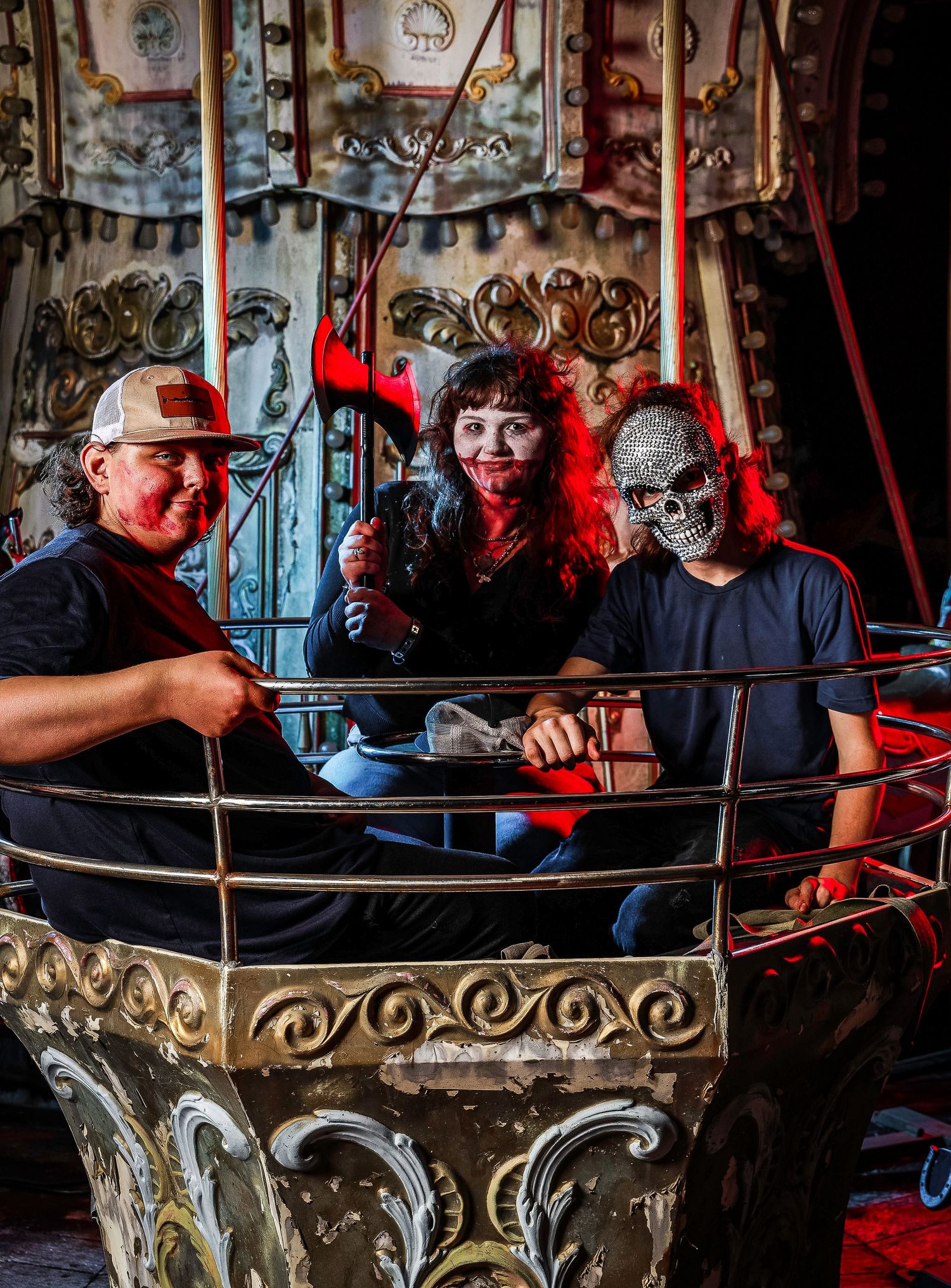 Three people pose together on an ornate vintage carousel ride with decorative gold details and poles.