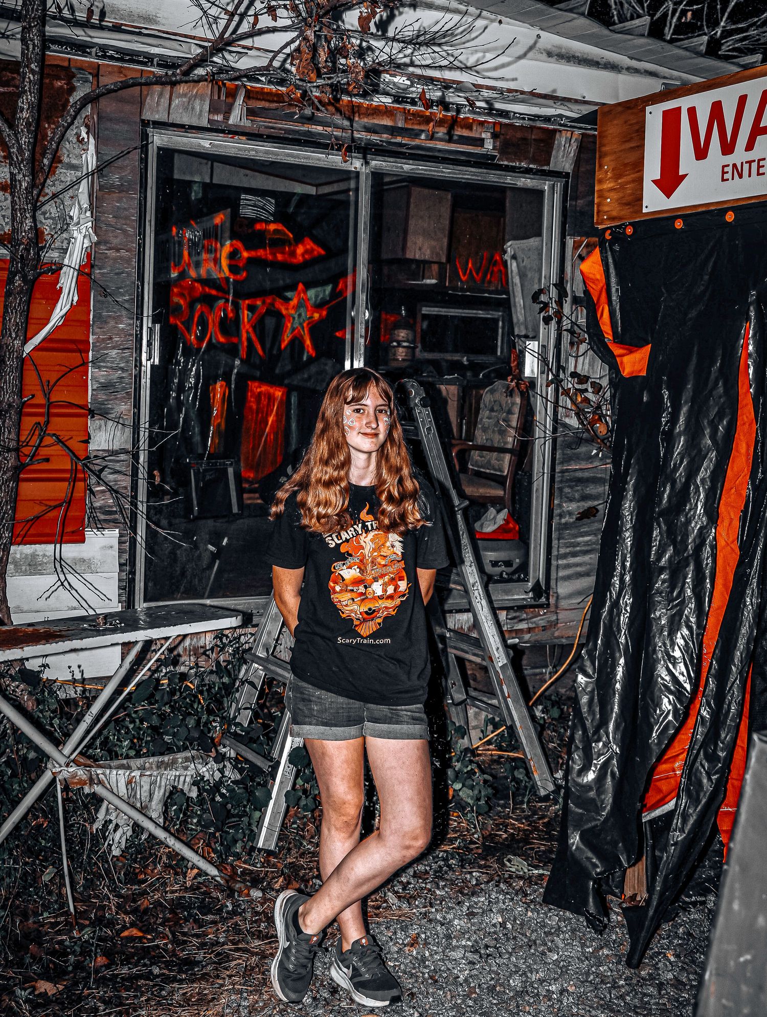 Dark Halloween scene with spooky decorations and someone wearing a black t-shirt with orange graphic in a dimly lit space.